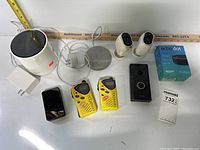 Overview of multiple electronics on white table including speakers, walkie talkies, smartwatch, and doorbell