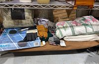 Photo showing assorted homegoods on a shelf including blankets, gloves, a quilt, and organizers.