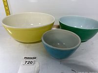 Front view of three vintage Pyrex mixing bowls in yellow, green, and blue colors.