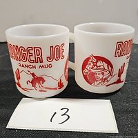 Front and side view of the two white glass mugs with red printed graphics reading 'Ranger Joe Ranch Mug' by Hazel Atlas.