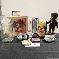 Full view of all collectibles showing glass jar, framed pins, ceramic birds, basket, spoon, nesting doll, cup, dish, packet, and metal sculpture