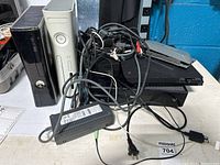 Four Xbox gaming consoles and a pile of assorted cables and accessories placed on a table.