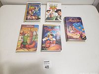 Five Disney adventure movie VHS tapes on a white surface: Toy Story, Toy Story 2, Aladdin, Robin Hood, and Pinocchio