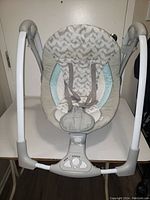 Front view of baby rocker showing cushioned seat with chevron pattern and safety harness.