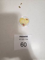 The coin viewed from a distance with the case to show size and context, placed on a surface next to lot identifier card.