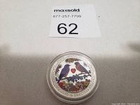 Photo of the coin showing colorful birds, heart, and floral elements with 'Love is Precious' inscription