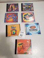Photo of seven dance music CDs in jewel cases arranged flat on a white surface. Covers show multiple titles of 1990s and 2000s dance music compilation albums.