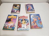 Five Disney VHS tapes laid out on a white surface showing front covers of The Fox and the Hound, Song of the South, Pocahontas, Pocahontas II, and Hercules