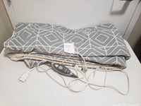Gray and white geometric patterned electric heated blanket folded with visible control wires and unit on a white surface.