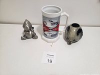 Photo of the three items in the lot including the coffee mug centered, silver-tone dragon bank right, and silver-tone elephant figurine left.
