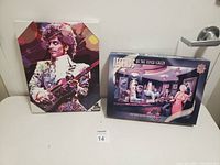 Photo of the Prince art print and Elvis puzzle box together on a surface with a lot number card in front