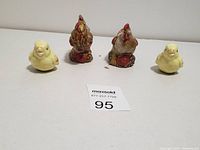 Front view of four salt and pepper shakers shaped as two roosters and two chicks, arranged in a row on a white surface.