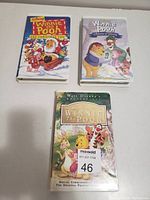 Photo showing three Disney Winnie the Pooh VHS movies with colorful illustrated covers including Christmas, Seasons of Giving, and Classic collection.