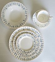 Overhead view of a full 6-piece place setting including cup and saucer, bowl, dinner, salad and side plates, showing the floral pattern and gold rim detail.