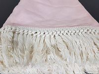 Close-up photo showing soft pink linen fabric and knotted white fringe tassels on the edge of the tablecloth.