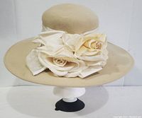 Front view of the beige wool hat showing the crown, wide brim and cream fabric floral decoration tied with a wide band.
