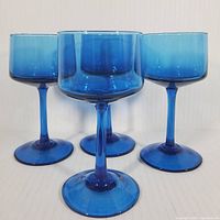 Four aqua blue crystal goblets with cylindrical bowls and stems shown in a group.