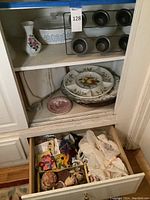 Full view inside cabinet showing multiple kitchen and serving items including platters, muffin pan, Corningware casserole dish, shells, and linens.