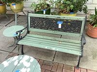 Wood and metal bench with weathered green paint and cast iron backrest and armrests, showing overall condition and size.