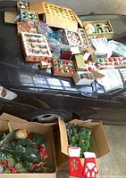 Wide view of all boxes containing vintage Christmas ornaments, greenery, and stockings arranged on a car hood.
