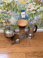 Full lot showing fondue pot with lid and stand, pour-over coffee maker with paper filter, metal stovetop coffee pot, and coffee scoop on wood floor with floral wallpaper background.