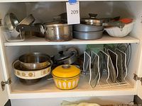 Overview of issued cookware including pots, pans, a lid organizer, mixing bowls, and bakeware molds inside a cabinet.