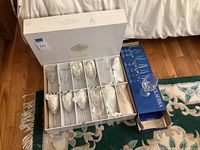 Full set of 12 Shannon Crystal Dublin lead crystal wine glasses in original white box with individual compartments and tissue wrapping, alongside a separate blue Claudia brand box containing one additional wine glass.