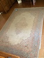 Full view of loom made rug on wooden floor showing muted each in central area and floral border