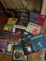 Multiple vintage LP vinyl albums arranged on wooden floor, showing cover art and titles mostly readable.