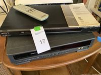 Sony DVD player on top of Hitachi VHS player, remote control and user manual on top of DVD player.