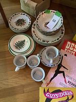 Overview of the Spode and Gibson Christmas china plates, bowls, cups, and saucers arranged on the floor showing holiday motifs and quantity.