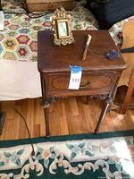 Wooden vintage side table with drawer, small framed mirror, wax seal press, and decorative tassel item on top