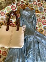 Full view of powder blue vintage dress hanging beside white tote bag on floral bedspread.
