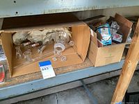 Box containing assorted laboratory glassware such as beakers, tubes, adapters, alongside a second box with electronic components, wires, switches.