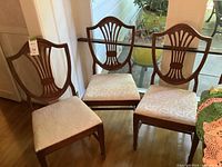 Set of six wooden dining chairs, one has arms. Chairs have cream brocade fabric seats and carved wooden backs.