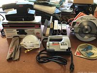 Photo showing SKIL belt sander, safety helmet, jigsaw, and Black & Decker circular saw on table with accessories.