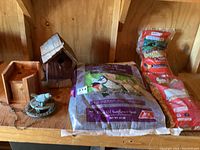 Overview photo showing two wooden bird houses, 20 lb bag of black oil sunflower seed, two additional bags of wild bird food, and small decorative bird feeder dish with bird figurine.