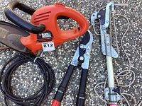 Electric hedge trimmer in orange and black with attached power cord, branch lopper, and extension pole lopper side by side on pavement.