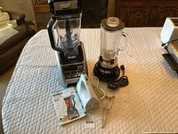 Ninja 1200 blender with manual, Waring Pro blender with glass jar and black base, all placed on quilted surface.