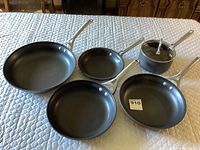 All cookware items laid flat with handles facing outward, showing the cooking surfaces and the glass-lidded stock pot.