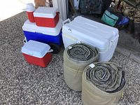 Coolers and sleeping bags arranged outside garage showing condition and quantity