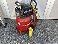 Red Craftsman air compressor with pressure gauges, hoses, and black motor housing photographed outdoors on pavement.