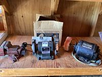 Showing the bench vise, Craftsman bench grinder, vintage Wagner motor all together on wooden workbench with grinder's original box in background.
