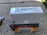 Photo of white Deluxe Radiant Heater placed on its original box outdoors, showing the top with control knobs and attached power cord.