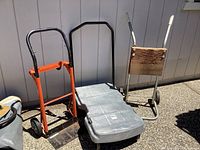 Photo of three dollies showing orange metal platform dolly, grey plastic platform dolly, and metal frame dolly with wooden platform distinct in size and construction