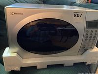 Front view of Emerson microwave oven showing silver finish with black oval door and side control panel with numeric and functional buttons.