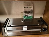 Front view of the GameSaver Titanium vacuum sealer with FoodSaver user manual on top.