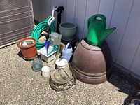 Photo showing assortment of garden pots, watering cans, glass globes, garden hose and other accessories on ground outdoors