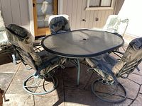 Outdoor patio set including oval glass top table and four swivel rocking chairs with cushions on green metal frames