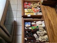 Open drawer showing multiple brown and white extension cords bundled with blue ties, electrical socket adapters and small boxed electrical accessories.